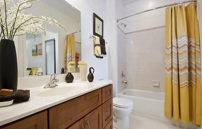 A bathroom with a white toilet, a sink with a brown towel, and a yellow shower curtain.