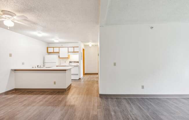 the living room and kitchen of an apartment with white walls and wood flooring