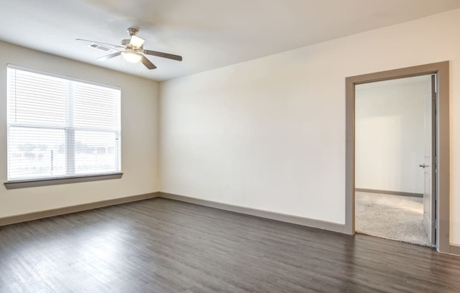 an empty living room with a window and a ceiling fan