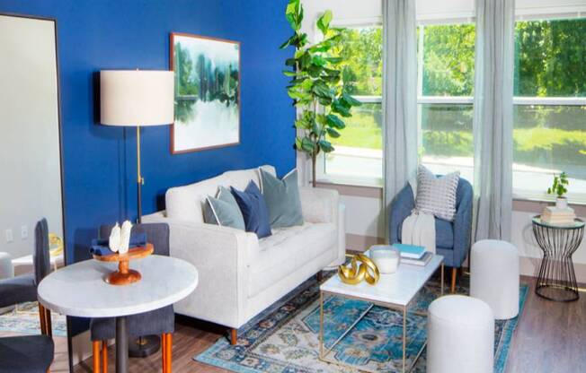 A living room with a white sofa, a round table with a lamp, and a blue rug.