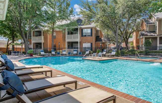 A pool surrounded by lounge chairs and trees.