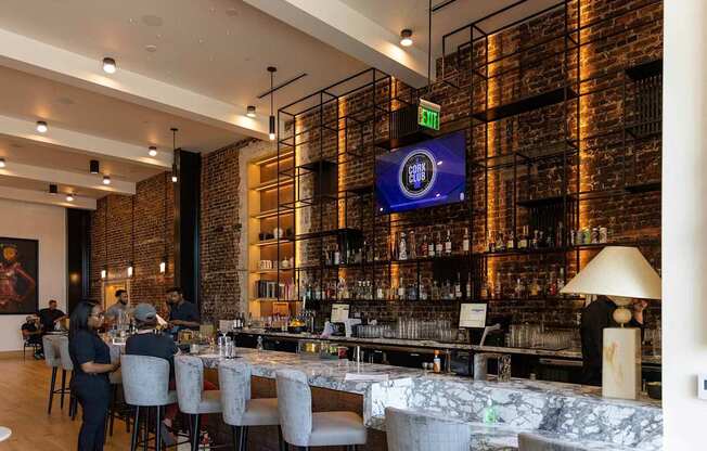 A bar with people sitting at the bar and a TV screen on the wall.