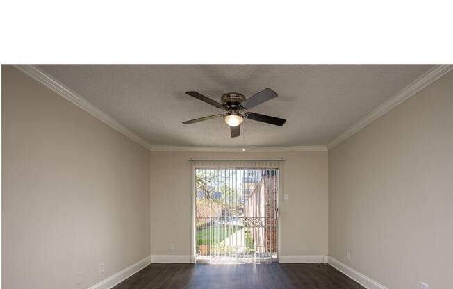 A room with a ceiling fan and sliding glass door.