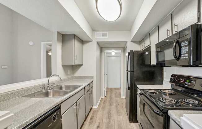 A kitchen with black appliances and a wooden floor.