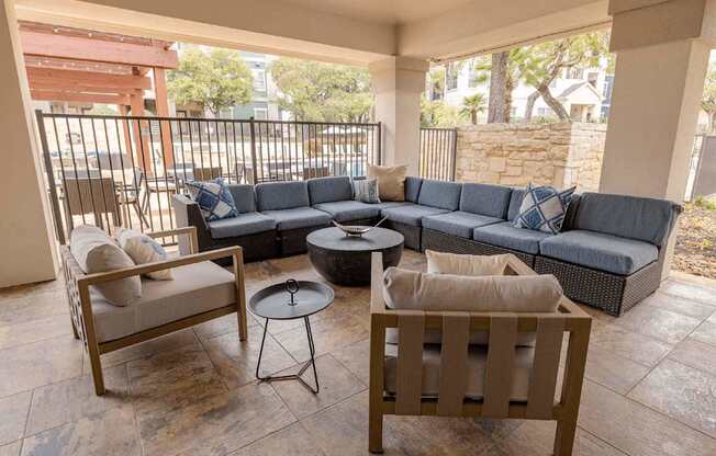 A patio with a grey couch, a wooden chair, and a round table.