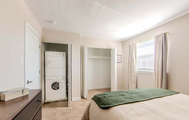A bedroom with a bed, a washing machine, and a refrigerator in the kitchen area.