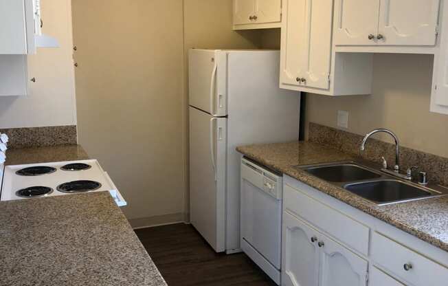 Kitchen with spacious white cabinets, plank style flooring, refrigerator, dishwasher, microwave, and electric stove at Plaza Verde Apartments in Escondido, California.