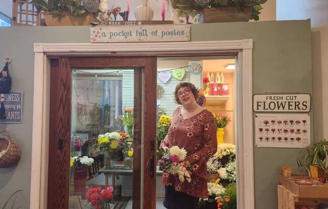 a woman standing in a flower shop holding a bouquet of flowers