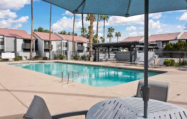 A pool area with a table and chairs and a building in the background.