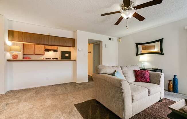 A living room with a beige couch and a ceiling fan.