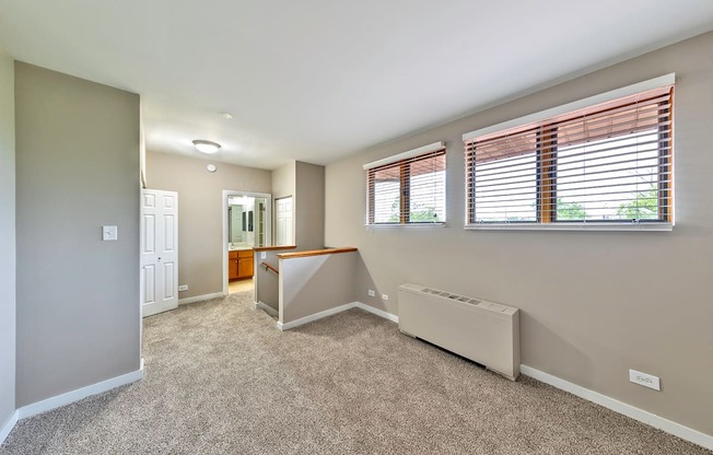 A room with a carpeted floor, a window with blinds, and a white radiator.