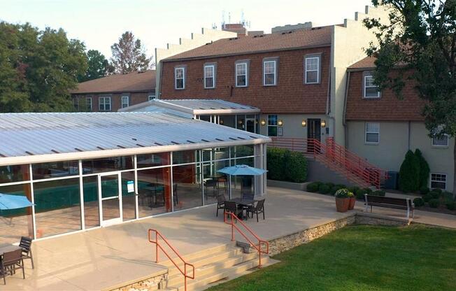 A patio with a table and chairs is surrounded by a grassy area and a building.