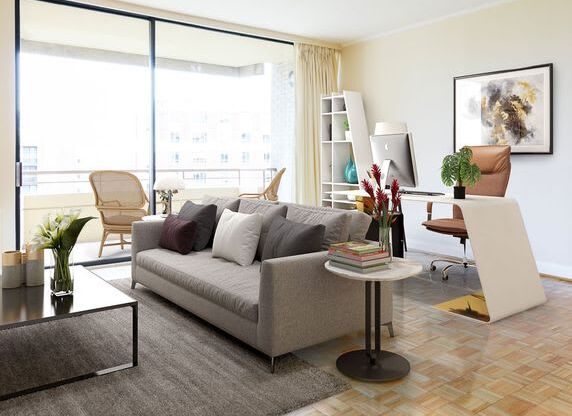 A living room with a grey couch, a coffee table, a chair, a potted plant, a bookshelf, and a painting on the wall.