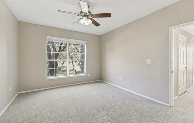 an empty bedroom with a ceiling fan and a window