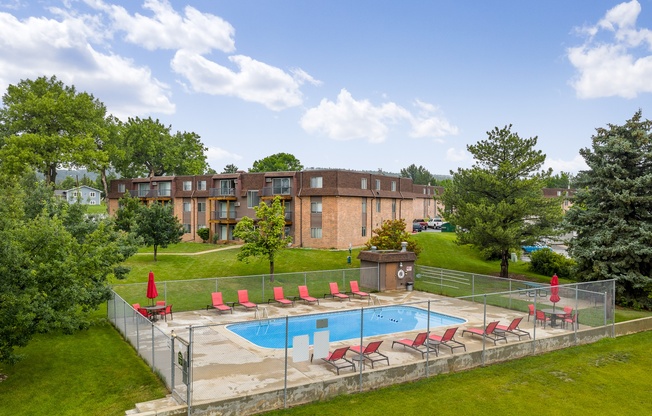 A pool surrounded by a fence with red chairs.