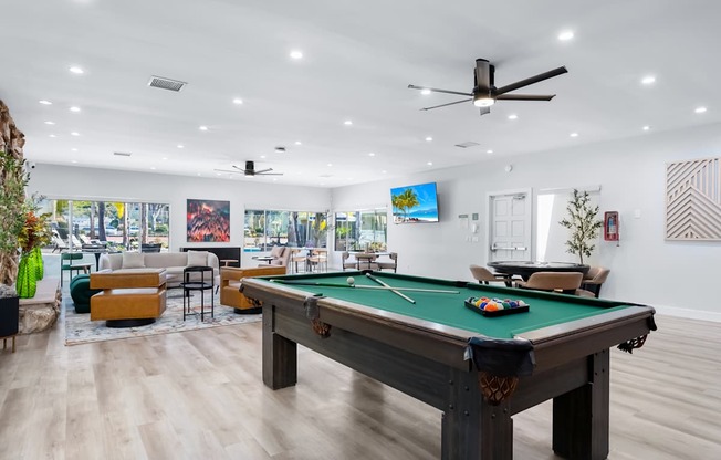 A pool table is in the middle of a room with a ceiling fan and a wall with pictures.