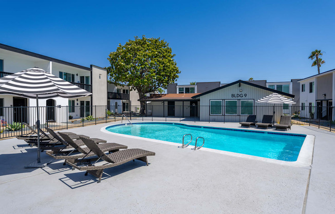 A pool with sun loungers and umbrellas in front of a building with BLDG 9 on it.