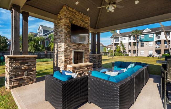 1 BR Apartments in League City, TX - Anchor at South Shore - Outdoor Lounge with Cozy Seating, a TV, a Fireplace, and a Ceiling Fan