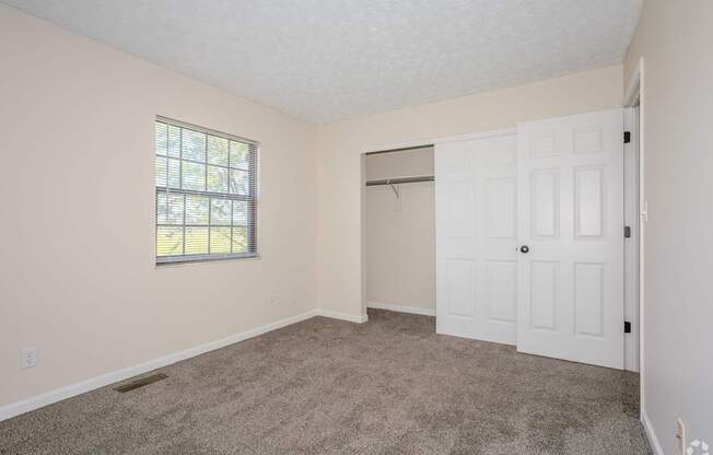 A room with a carpeted floor, a window with blinds, and a white door.