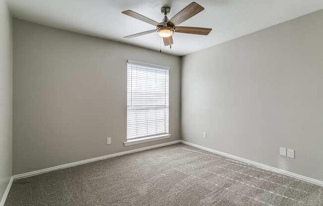 A room with a ceiling fan and a window with blinds.