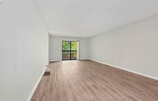 A living room with wooden flooring and a window with a view of trees.