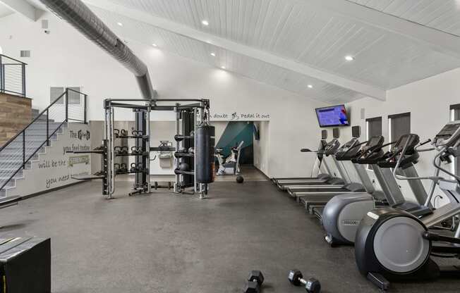 a gym with cardio equipment and weights on the floor and a staircase