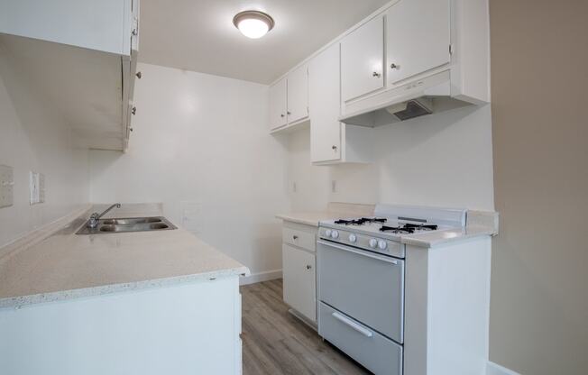 an empty kitchen with white cabinets and a stove and a sink