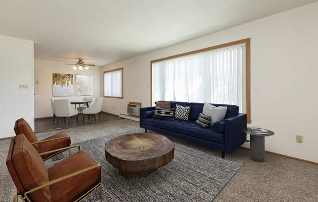 Fargo, ND Islander Apartments. A living room with a blue couch and leather chairs. A large window brightens the room with natural light.