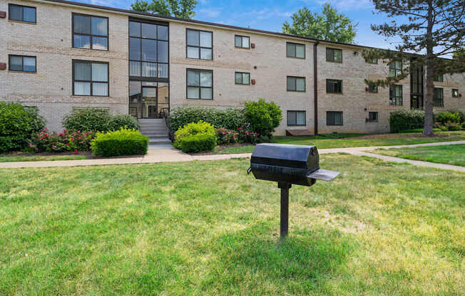 A black mailbox sits on a green lawn in front of a brick building.
