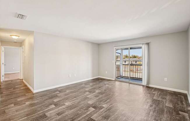 A room with a wooden floor and a sliding glass door leading to a balcony.