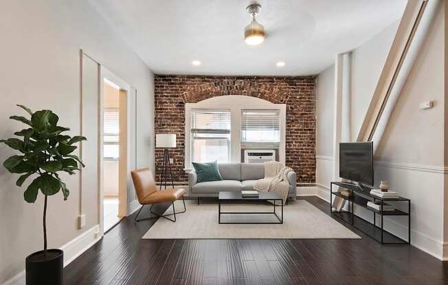 A living room with a brick wall and a grey couch.