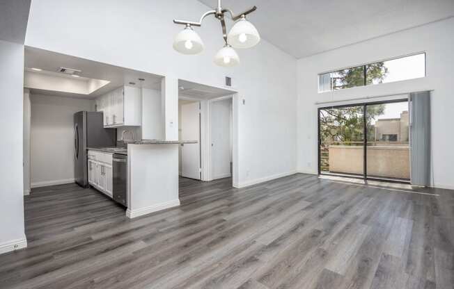 an empty living room with a kitchen and a door to a patio