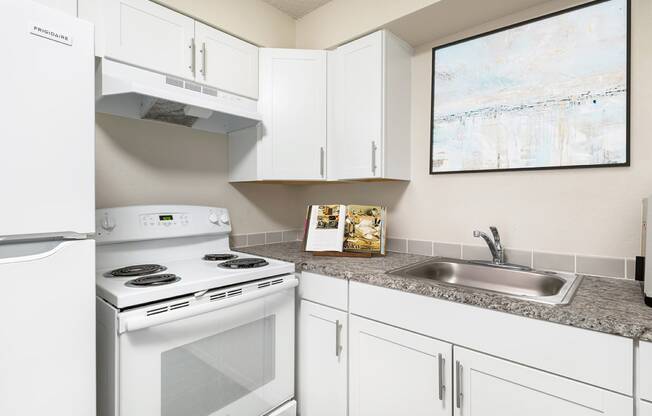 Corner of a kitchen with custom white cabinets, spacious countertops, a stainless steel sink, oven, stovetop and hood range, and full-size fridge.at Wildflower, Washington