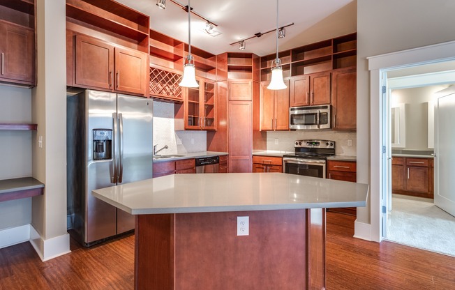 View of Kitchen, Showing Island, Stainless Steel Appliances, Plank Wood Flooring, and View of Bathroom at Alpha Mill Apartments