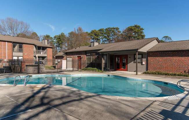 A swimming pool in front of a brick building with a red door.