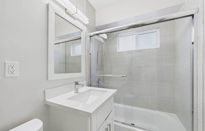 A white bathroom with a sink, mirror, and bathtub.