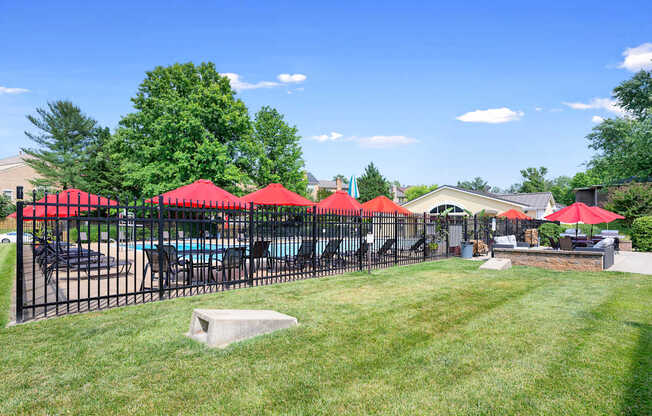 A pool surrounded by red umbrellas and a black fence.