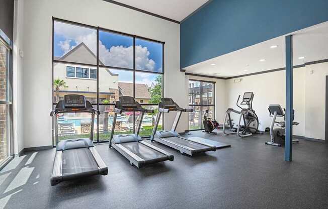 A gym with treadmills, exercise bikes, and a view of a pool and houses outside.