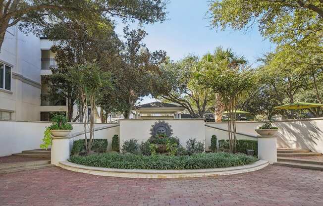 A courtyard with a circular brick walkway and a white wall with a planter in the middle.