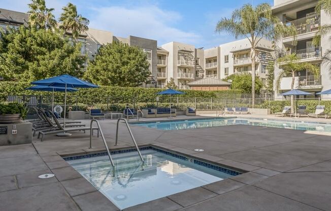 a swimming pool with chairs and umbrellas in front of an apartment building