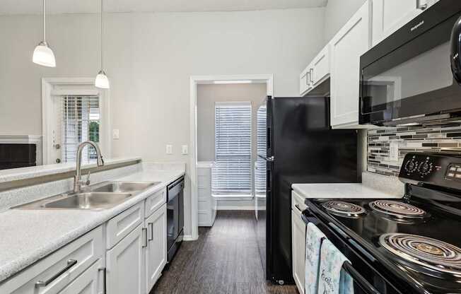 A black refrigerator sits in a kitchen with white cabinets and a black stove.