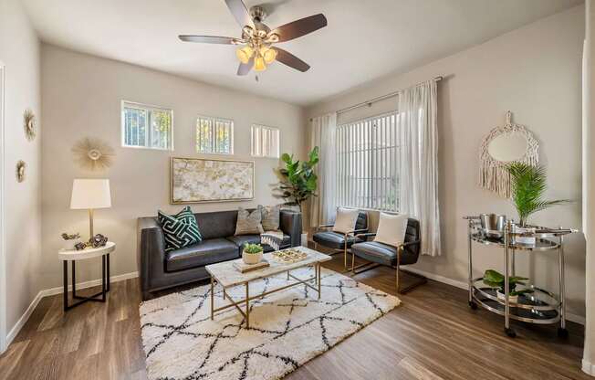 A living room with a grey couch, a coffee table, a ceiling fan, and a rug.