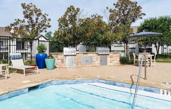 Poolside grilling area with two barbecue stations, lounge seating, and shaded outdoor table.