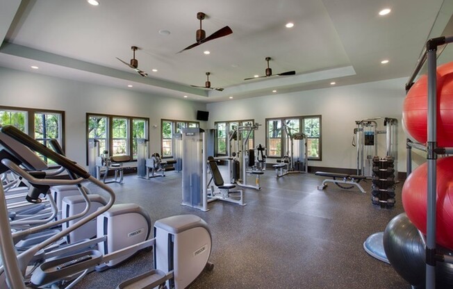 Photo of fitness center showing several elliptical machines, as well as 7 weight stations, and multiple free-weights and exercise balls.