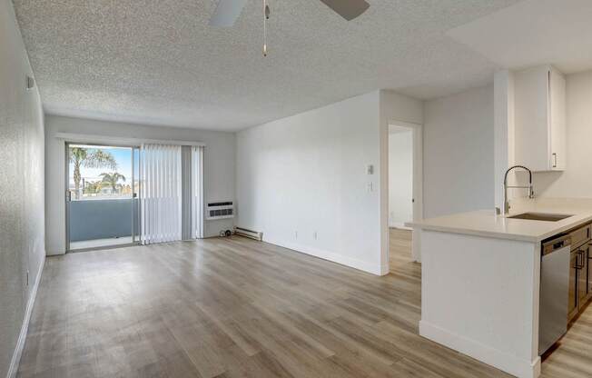 A spacious living room with a kitchenette and sliding glass doors leading to a balcony.