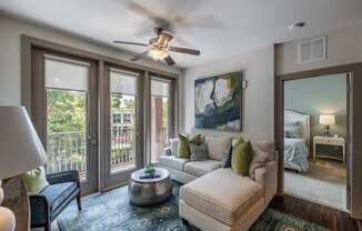 A well-lit living room with a ceiling fan and a view of the balcony.