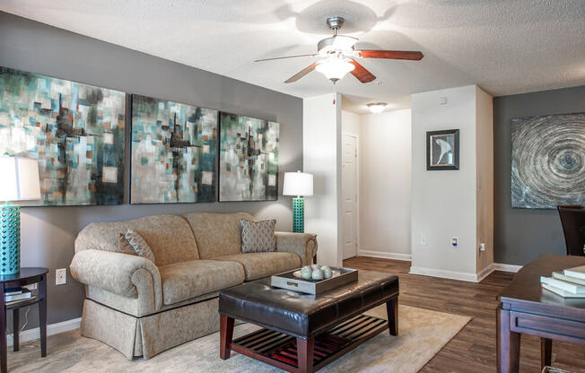 A living room with a beige couch, a coffee table, and a ceiling fan.