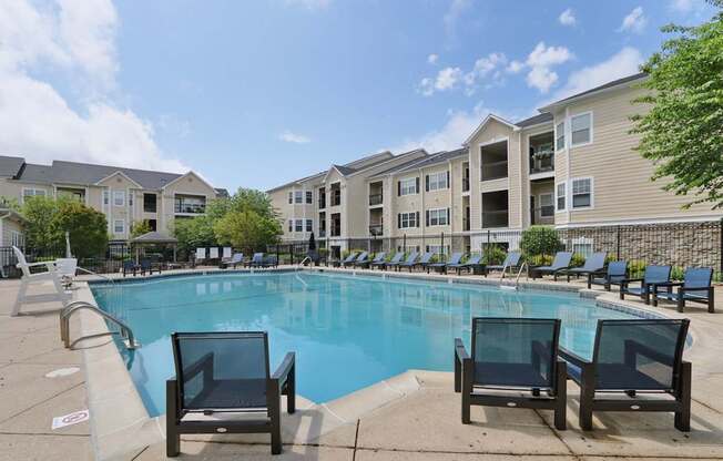A swimming pool surrounded by lounge chairs and apartment buildings in the background.