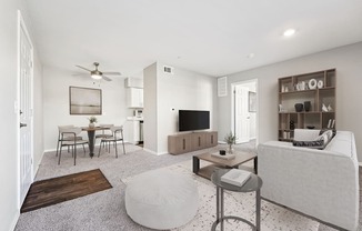 A living room with a grey sofa, a coffee table, a TV, a dining table, and a ceiling fan.
