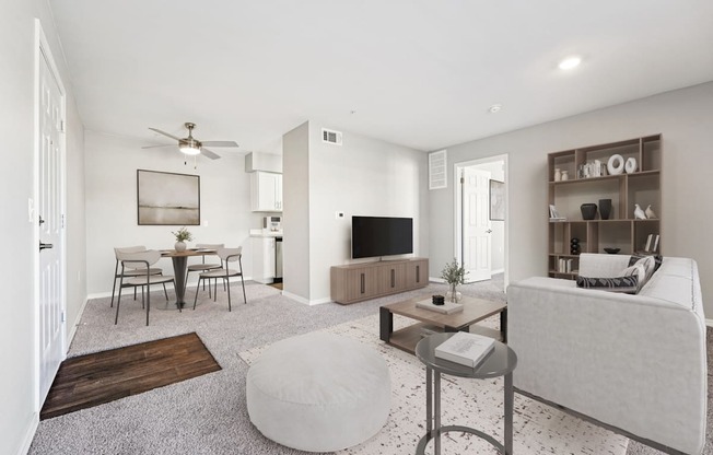 A living room with a grey sofa, a coffee table, a TV, a dining table, and a ceiling fan.